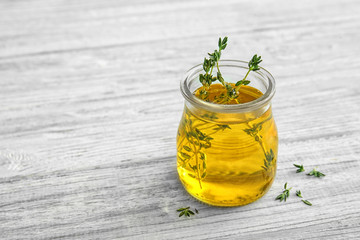 Oil with thyme in glass jar on light wooden background