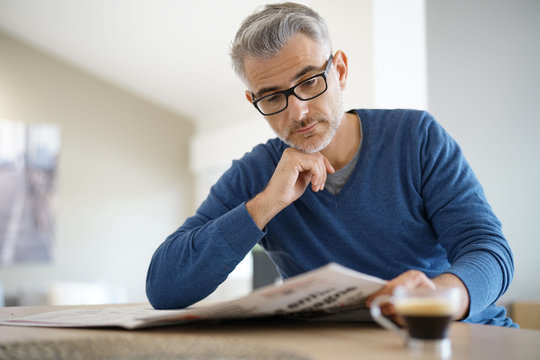 Middle-aged man at home drinking coffee and reading newspaper