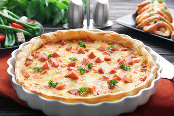 Delicious casserole with sausages in baking dish on table