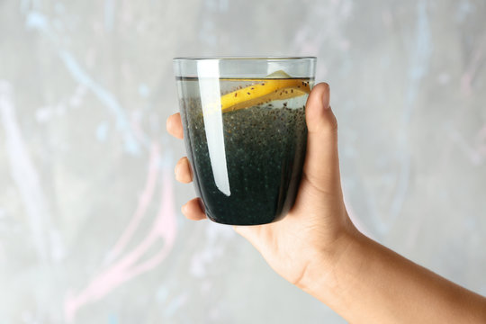 Hand holding glass of water with chia seeds and lemon on light background