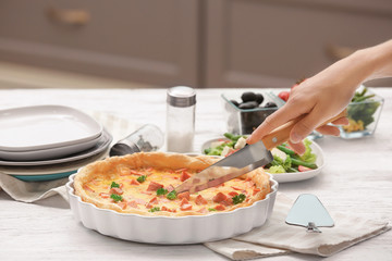 Woman cutting tasty casserole with sausages in baking dish on table