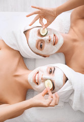 Young women with facial masks and cucumber slices in spa salon