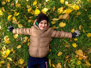 cheerful 4 years old boy lying on yellow leaves in autumn. top view © Saksoni