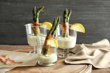 Glasses with bacon wrapped asparagus and sauce on table