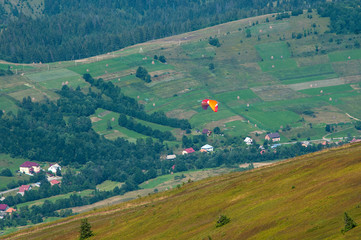 Paraglider flies over a mountain valley on a sunny summer day. Paragliding in the Carpathians in the summer.