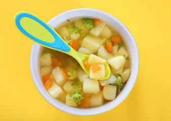 Bowl of delicious baby soup on yellow background