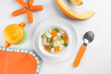 Composition with plate of delicious baby soup on white background