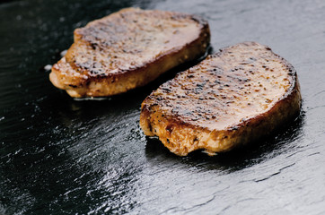 Grilled pork chops, steaks on a black slate. Fresh meat with foam. Dark background. Grilled and barbecue concept.
