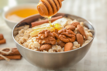 Tasty oatmeal with honey and nuts in bowl, close up