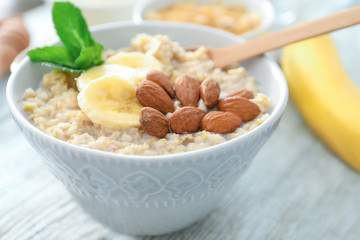 Tasty oatmeal with almonds and banana in bowl on table, close up