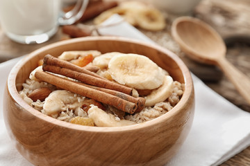 Tasty oatmeal with banana and cinnamon sticks in bowl on table