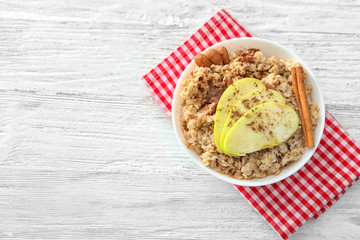 Tasty oatmeal with apple and cinnamon in bowl on table