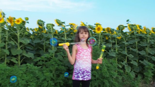 Happy child on a field of sunflowers with soap bubbles. A little girl blows bubbles.