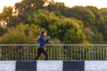 Young sporty woman jogging on bridge in the morning. Running fitness girl in sportswear outdoor image with copy space