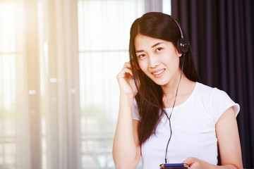woman in headphones listening to music from smartphone with window background