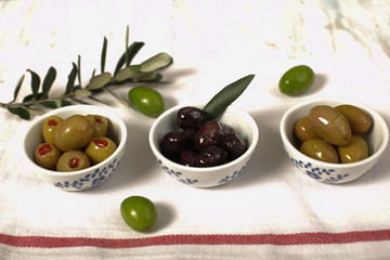 Three kind of olives and young olive branch on cloth napkin over old wood background