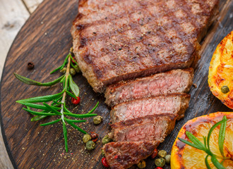 Sliced grilled beef barbecue steak with lemon, rosemary and spices on cutting board closeup. Selective focus