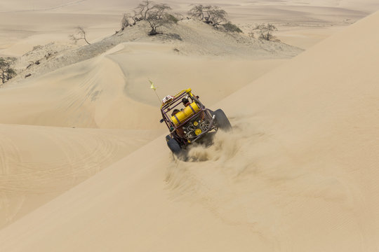 Dune buggy with passengers speeding across the side of a large d