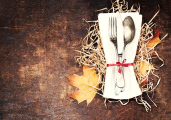 Dinner plate setting top view with Thanksgiving decorations on old wooden table. Seasonal cutlery on Autumn background..