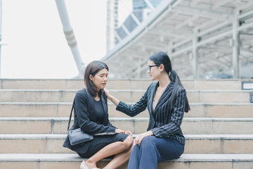 Tired two asian businesswomen are sitting on stair outside office after working hard, headache from work