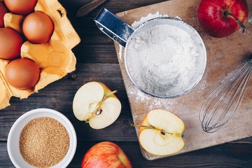 Ingredients for apple pie cooking with fresh red apples, flour, eggs, brown sugar and spices