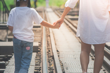 Adorable Family Concept : Woman and children walking on railroad tracks and holding hand together with looking to forward in vintage style.