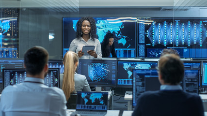 Chief Project Engineer Consults Tablet Computer and Holds Briefing for a Team of Scientists that are Building Machine Learning System. Displays Show Working Model of Neural Network.