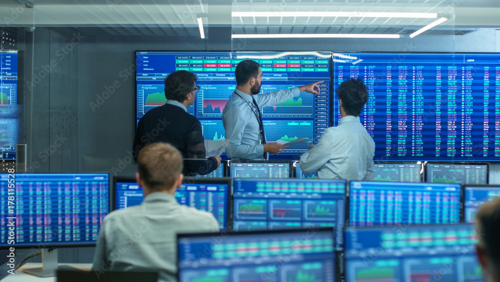 Poster Three Experienced Stock Traders Talking Business, Consulting Documents and Argue About Data. They Work for a Big Stock Exchange Firm. Office is Full of Displays Showing Infographics and Numbers.