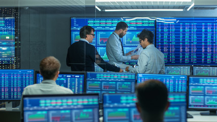 Three Experienced Stock Traders Talking Business, Consulting Documents and Argue About Data. They Work for a Big Stock Exchange Firm. Office is Full of Displays Showing Infographics and Numbers.