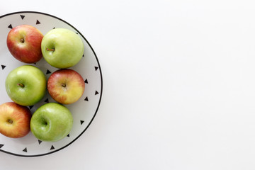  Top view of Red and green apples in white plate with black triangles pattern on the left side with white background.