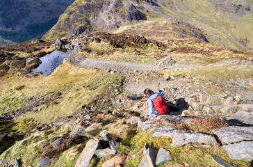 A female hiker and their dog descending a rocky path from the summit of Hay Stacks in the English...