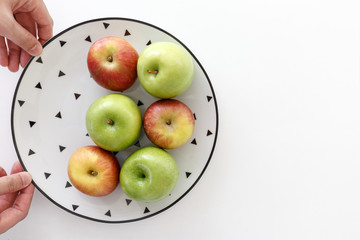Top view of Red and green apples in white plate with black triangles pattern with hands on the left side with white background.