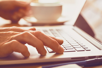 A closeup of an office worker using a computer keyboard, laptop on a sunny morning, evening.