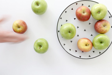Top view of Red and green apples in white plate with black triangles pattern and apples with moving hand  on white background.