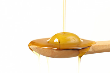 Close up view of virgin olive oil pouring on wooden  spoon on white background