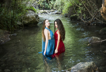 Fototapeta premium Two beautiful women on the bank of a mountain river with evening dresses