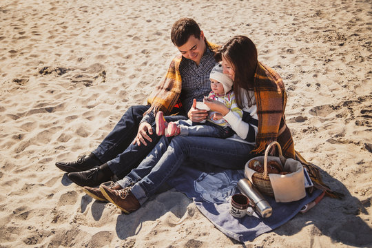 Young Happy Loving Family With Small Child At Picnic, Enjoying Time At Beach Sitting And Hugging Near Ocean, Happy Lifestyle Family Concept