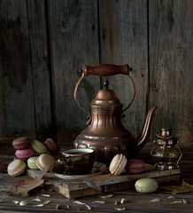 Vintage copper coffee pot, cup of black coffee and colorful macaroons on rustic wooden background....