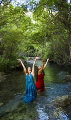 Two beautiful women on the bank of a mountain river with evening dresses
