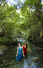 Two beautiful women on the bank of a mountain river with evening dresses