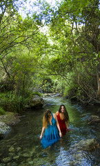 Two beautiful women on the bank of a mountain river with evening dresses