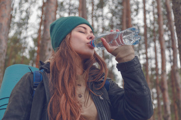 Hiker girl enjoying water. Happy woman tourist with backpack drinking water from bottle in nature.