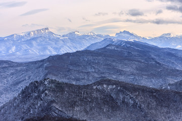 Beautiful scenic winter mountain landscape of Lagonaki mountain region with snowy peaks and forest valley. Bolshoy Tkhach mountain peak on background. Caucasus, Russia