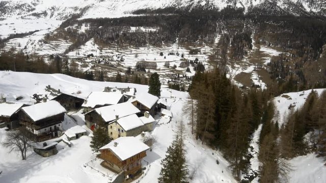 Winter aerial drone establisher over snowy town and forest woods valley under iced mountains.Snow in mountain nature outdoors.Down flight. Travel exploring Alps. 4k top view video