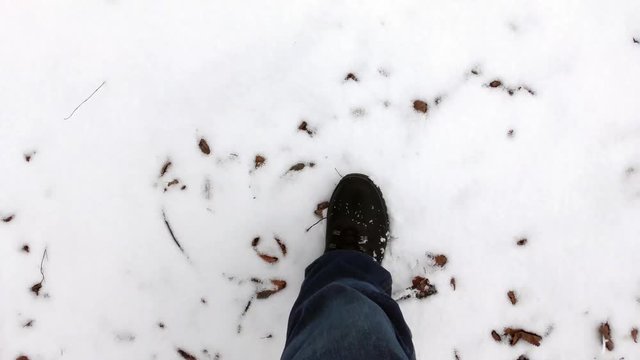 the feet of the man in black boots walking on snow