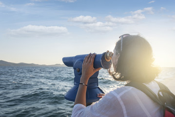 Obraz premium Young woman looks in a telescope or binoculars by the sea.