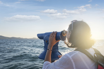 Young woman looks in a telescope or binoculars by the sea.
