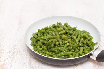 green beans on frying pan on wooden background