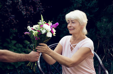 Elderly woman get a beautiful bouquet of field flowers. Smiling senior lady holding a bunch of flowers.  Close up of senior's hands holding a posy.