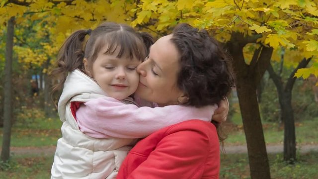 Woman with child in the park. Little girl hugging mother in an autumn park.